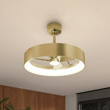 A modern ceiling fan with a circular gold frame and integrated LED light, mounted on a white ceiling in a contemporary room with wood paneling and a window with horizontal blinds.