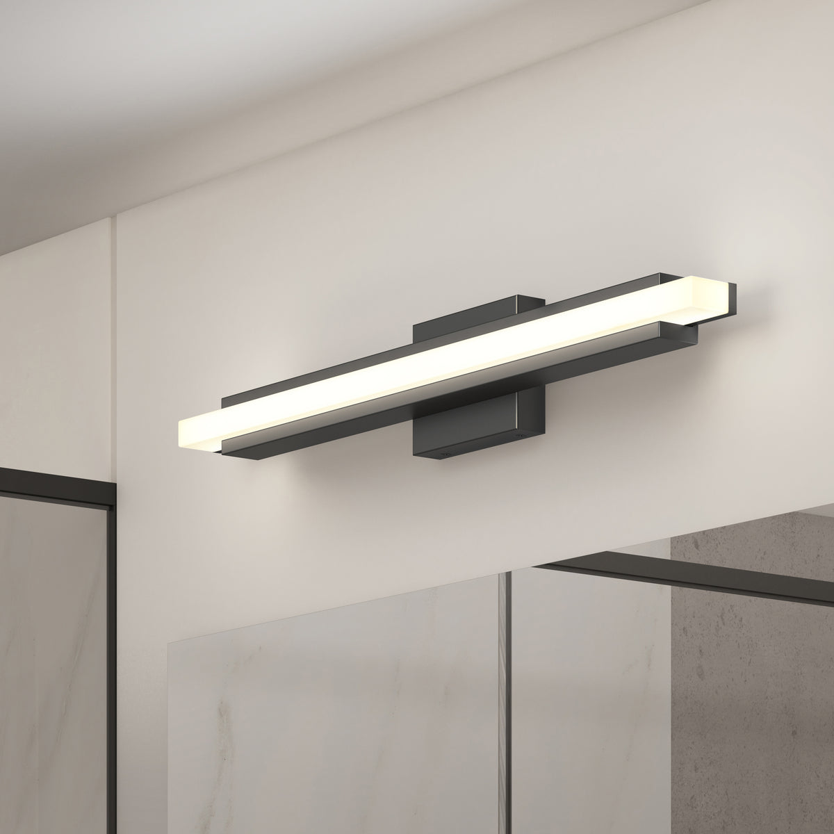 A modern rectangular LED wall light with a black base is mounted above a bathroom mirror on a light-colored wall. The light emits a soft, even glow.