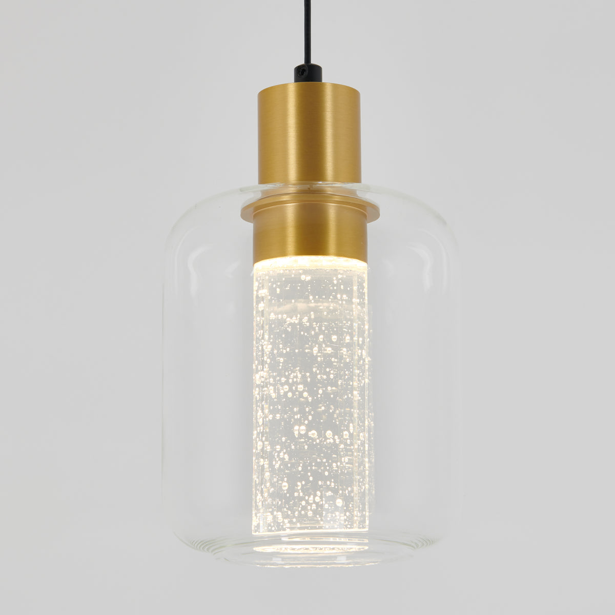 A modern pendant light with a cylindrical clear glass shade, a gold metal fixture, and an illuminated inner glass tube filled with small bubbles, hanging from a black cord against a light gray background.