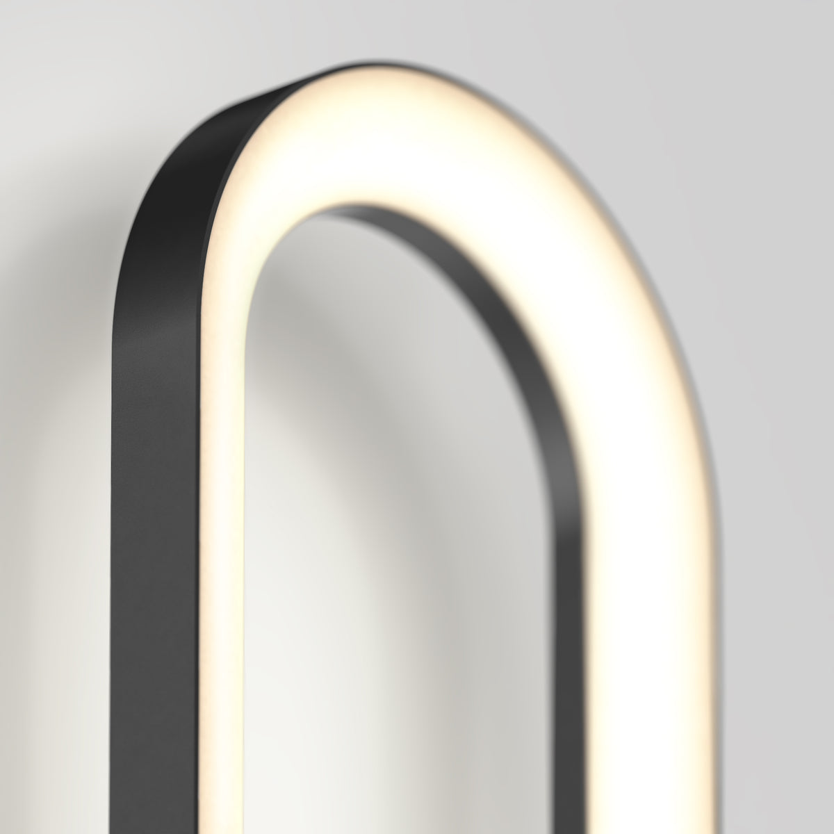 A close-up of a modern, oval-shaped wall light fixture with a black frame and a glowing white LED strip, mounted on a light gray wall.