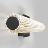 A cylindrical wall-mounted light fixture with a textured, crystal-like surface emits a soft, warm glow against a plain light gray background.