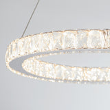 A close-up of the Artika Celebrity LED pendant light, a modern circular chandelier with crystal-like segments, emitting bright white light and suspended from the ceiling by thin wires against a light gray background.
