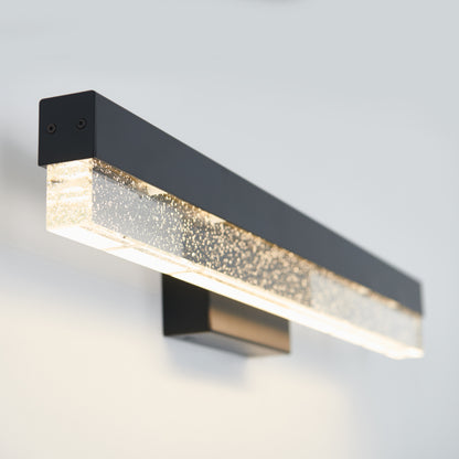 The Artika Bubble Bar LED bathroom vanity light features a modern wall-mounted design with a rectangular black frame and a bubble-filled clear section, casting a soft, warm glow against a light gray wall.