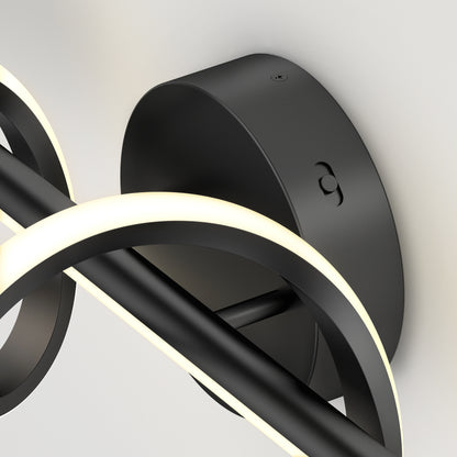 Close-up of the Artika Coda modern LED bathroom vanity light 5 CCT, a black wall-mounted fixture with curved LED strips emitting a soft white glow, attached to a round black metal base on a light-colored wall.