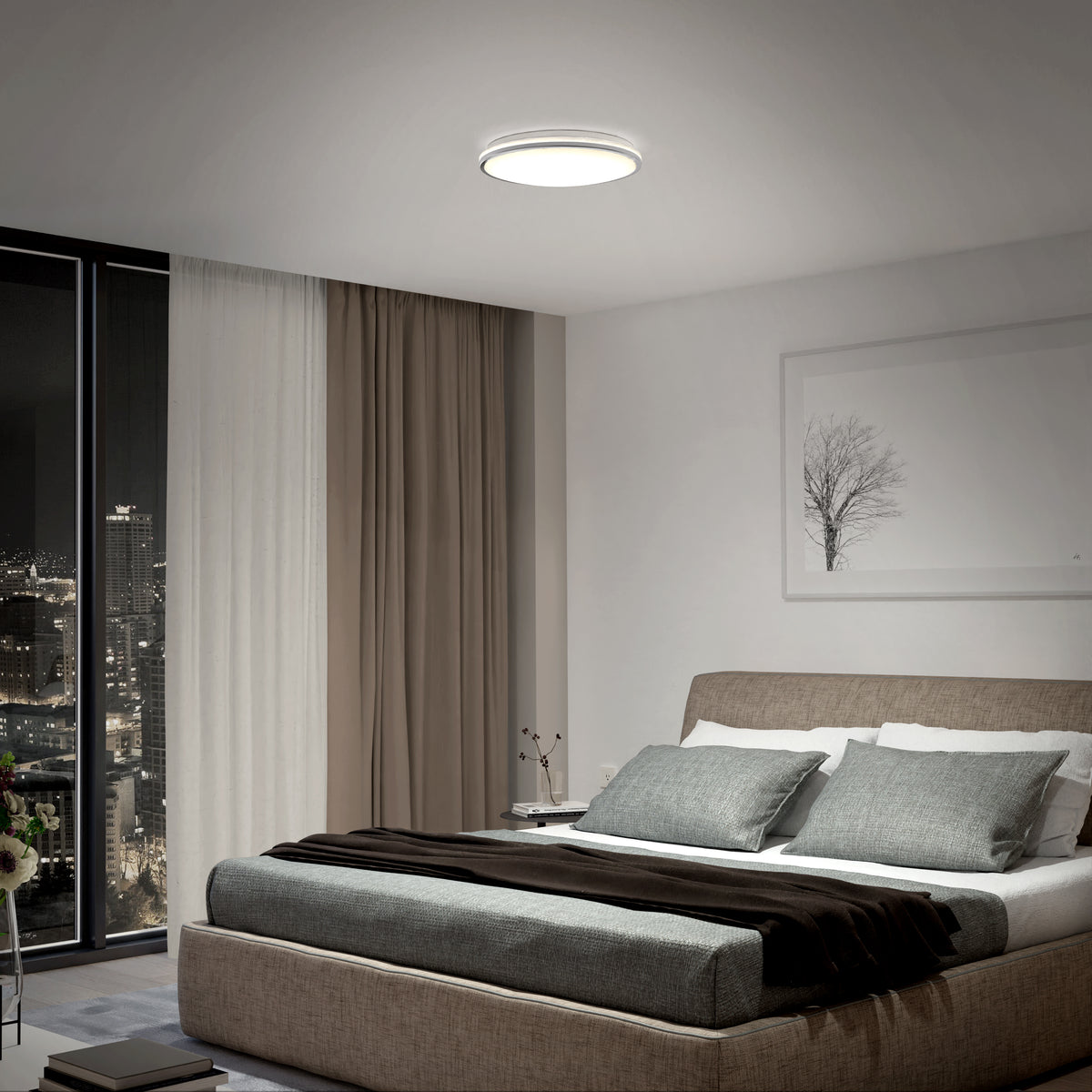 A modern bedroom features a large bed with gray and white bedding, floor-to-ceiling windows with city views, a sheer curtain, a framed tree artwork, and a round ceiling light illuminating the room.