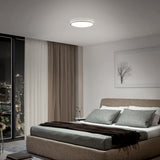 A modern bedroom features a large bed with gray and white bedding, floor-to-ceiling windows with city views, a sheer curtain, a framed tree artwork, and a round ceiling light illuminating the room.