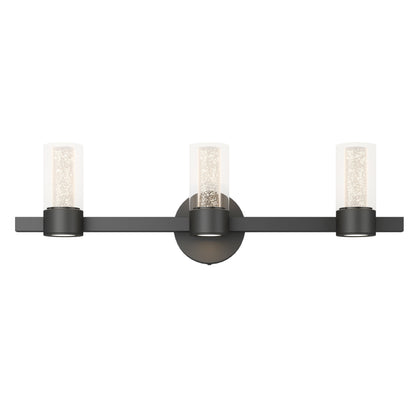The Artika Novello modern LED bathroom vanity light features three cylindrical clear glass shades with sparkling bubble details, a matte black horizontal bar, and a circular wall mount for contemporary style.