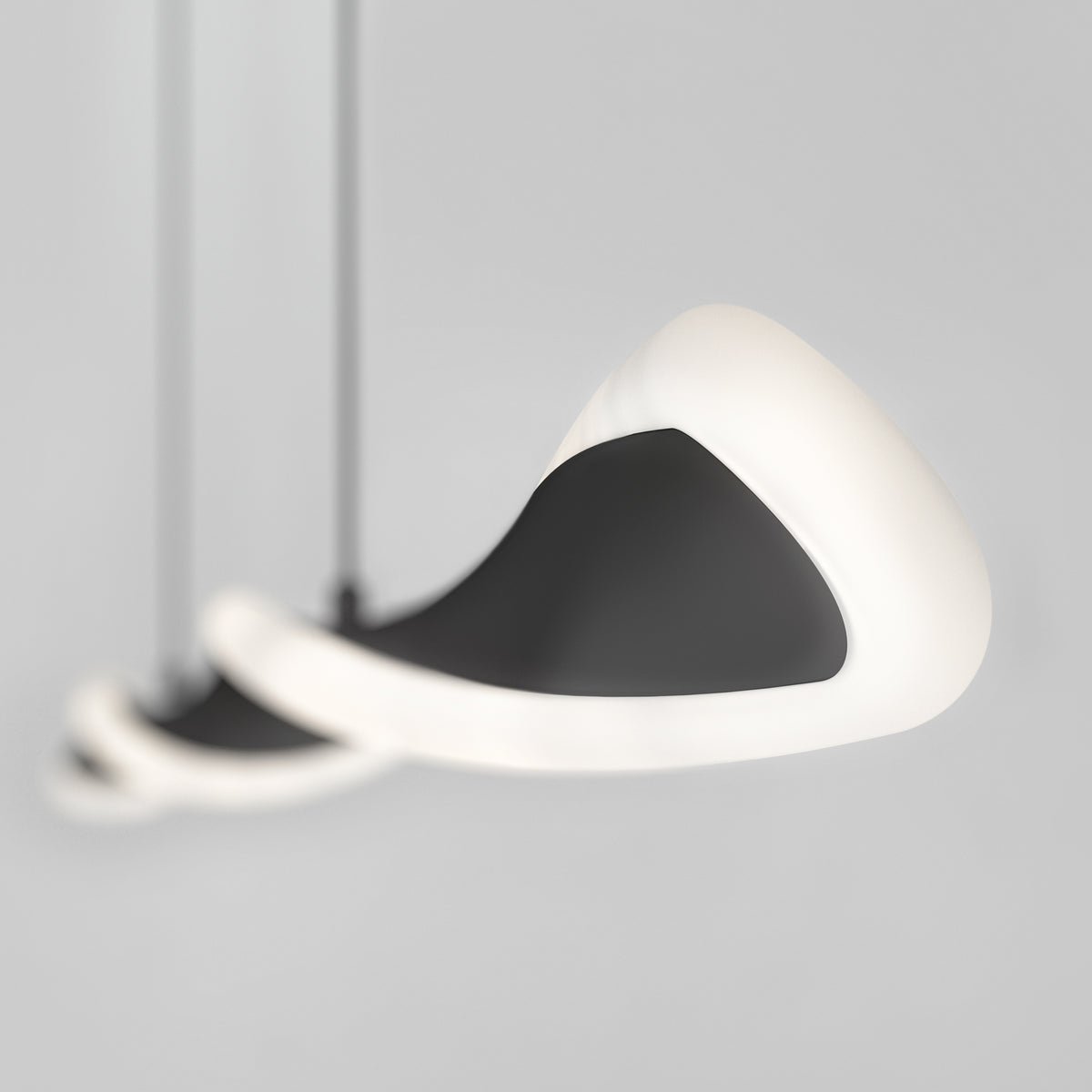 A close-up of three modern, abstract pendant lights with smooth black surfaces and glowing white edges, suspended against a plain light gray background. The lights appear to be floating in a spiral arrangement.