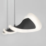 A close-up of three modern, abstract pendant lights with smooth black surfaces and glowing white edges, suspended against a plain light gray background. The lights appear to be floating in a spiral arrangement.