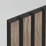 A close-up of a panel with alternating vertical strips of light wood grain and black material, viewed at an angle against a plain light background.