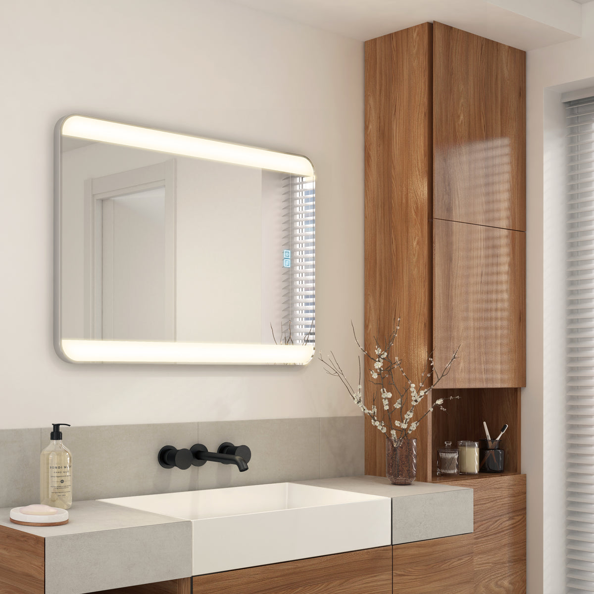Modern bathroom featuring the Artika Onyx 24″x32″ dimmable LED mirror, sink, wood cabinets, soap dispenser, and a vase with branches.