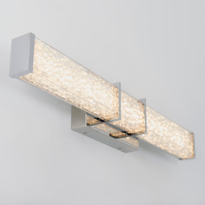 The Artika Royale LED bathroom vanity light features three rectangular bars with chrome accents and textured crystals, creating a soft glow when mounted on a light-colored wall.