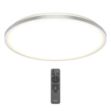 A round, modern ceiling light emits a soft white glow. Below it is a black remote control with multiple buttons for adjusting the light settings.