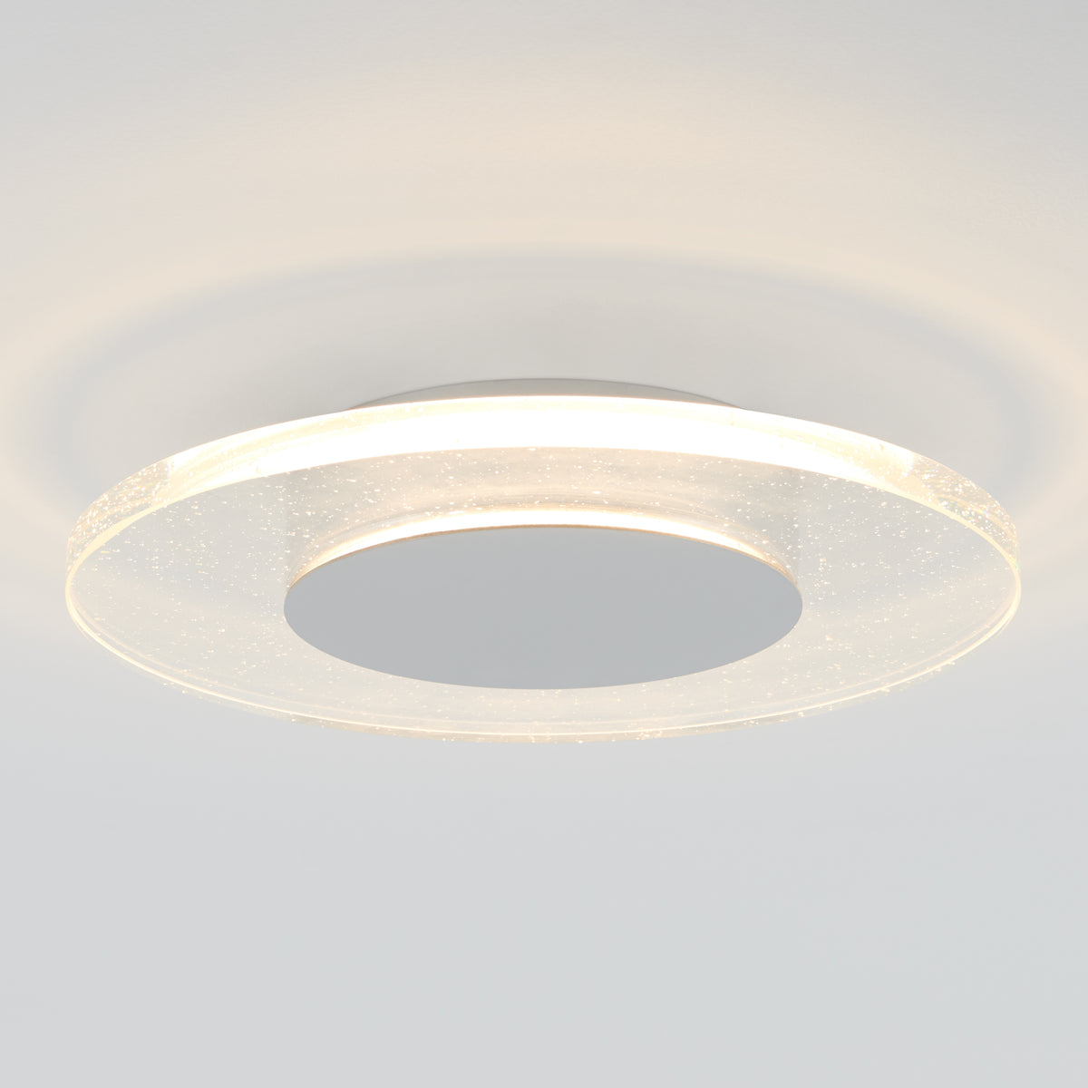 A modern circular ceiling light with a translucent, glowing ring and a solid central disc, mounted on a smooth white ceiling. The light creates soft, concentric shadows on the ceiling.