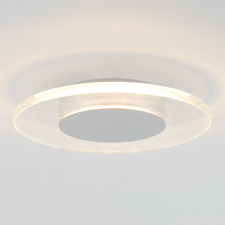 The Artika Essence Disk LED flush mount is a modern circular ceiling fixture featuring a glowing ring and metallic center, providing soft light and subtle reflections on the white ceiling.