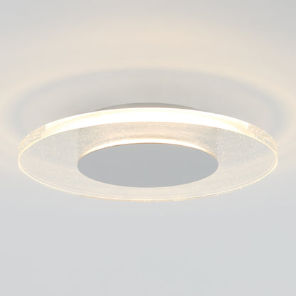 The Artika Essence Disk LED flush mount is a modern circular ceiling fixture featuring a glowing ring and metallic center, providing soft light and subtle reflections on the white ceiling.