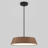 A modern pendant light fixture with a black rod and ceiling mount, featuring a wide, wood-textured lampshade and a glowing white interior, set against a plain light gray background.