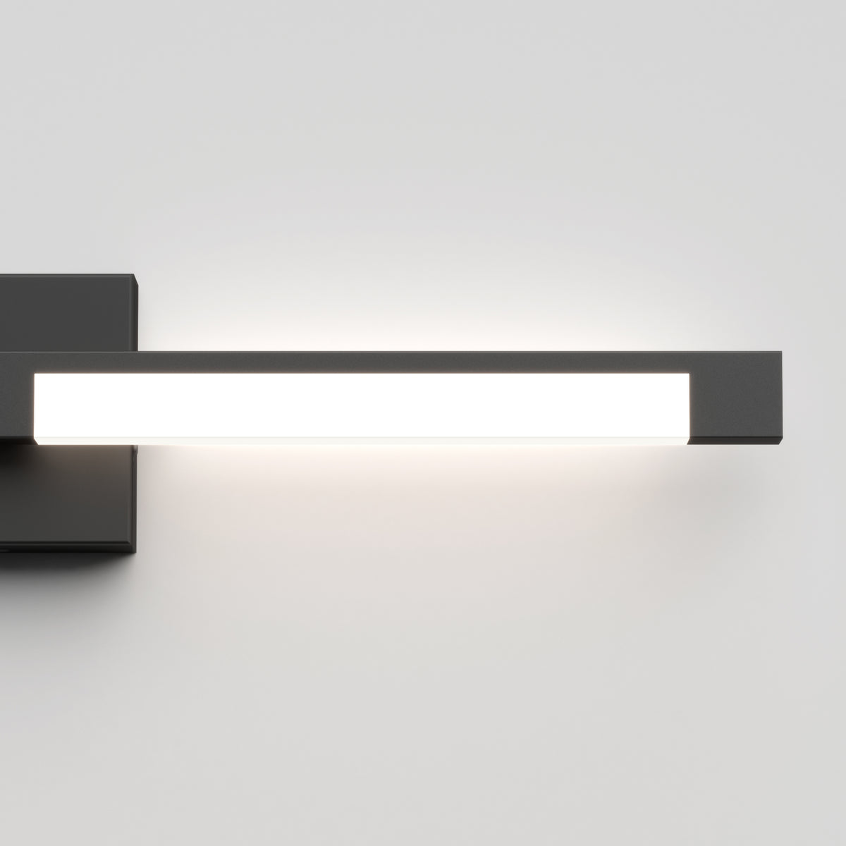 A modern, rectangular wall-mounted LED light with a black base and frame, glowing brightly against a plain white wall.