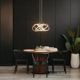 A modern dining area with a round wooden table, four black chairs, a decorative plant in a white pot, and an abstract pendant light, set against a black textured wall.