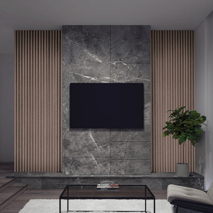 A modern living room wall features a mounted flat-screen TV, gray marble paneling, and Artika’s Panolok 30.67 ft wall panel kit (pack of 8) in oak finish as vertical slat panels, plus a potted plant, glass coffee table, and white Scandinavian rug.