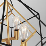 Close-up of a modern chandelier with exposed filament light bulbs in gold sockets, surrounded by intersecting black and gold geometric metal frames against a light background.