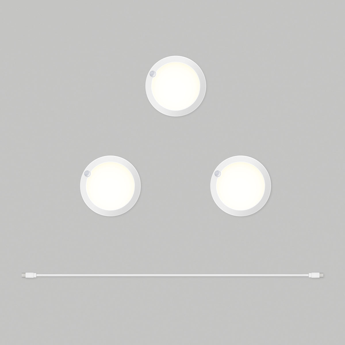 Three round, white puck lights arranged in a triangle on a gray background, with a single white USB cable laid horizontally below them.