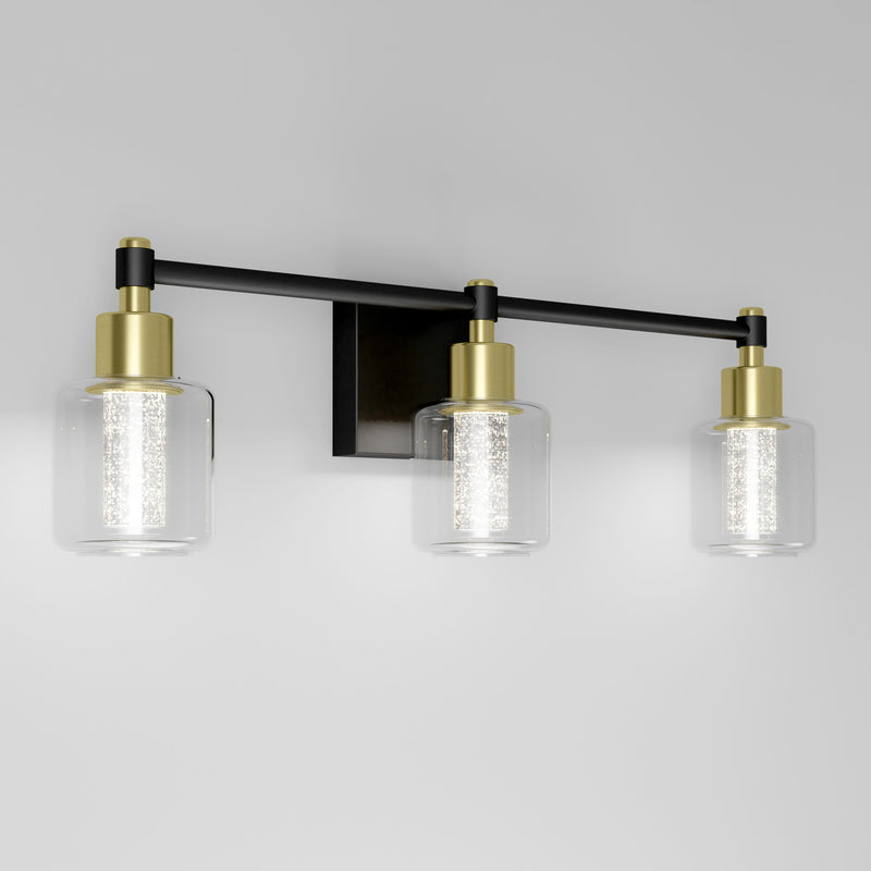 The Artika Champagne Globe bathroom vanity light features three LED lights with clear glass shades, gold accents, and a black base.