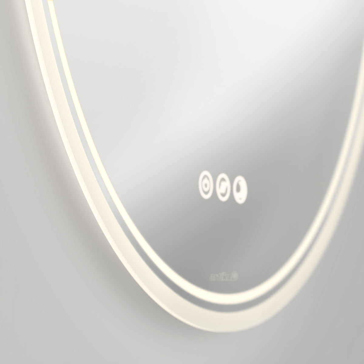 A close-up of a modern, round, backlit mirror with three illuminated touch control icons and a subtle brand logo on the bottom edge, set against a neutral background.