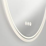 A close-up of a modern, round, backlit mirror with three illuminated touch control icons and a subtle brand logo on the bottom edge, set against a neutral background.