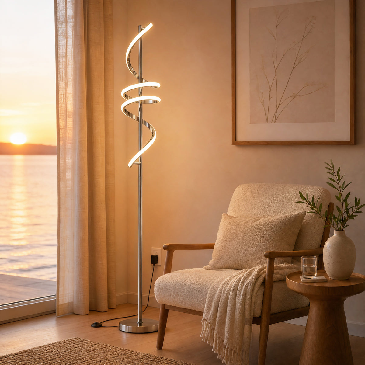A cozy living room features the Artika Coda modern LED floor lamp 5CCT, a blanket-draped armchair, a side table with water, and a large window revealing a sunset over the water.