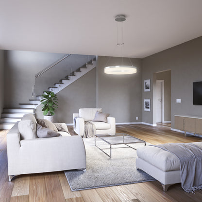 Modern living room with light-colored sofas, rug, coffee table, and the Artika Optical LED pendant light 3 CCT as a large ceiling fixture. Space features glass-railed stairs, potted plant, wall art, wooden floors, and neutral walls.