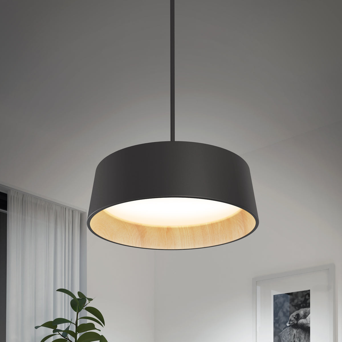 The Alton modern LED pendant light 5 CCT by Artika hangs in a minimalistic room with a leafy green plant, curtain, and framed artwork softly lit in the background. Its black finish features a light wood interior for added style.