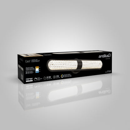 A rectangular black Artika box for the Carat LED contemporary bathroom vanity light 3 CCT displays an image of the illuminated fixture, features, and specs on the packaging, shown on a reflective gray surface.