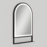 A wall-mounted, arched mirror with a black frame, built-in LED lighting around the edge, and a small black shelf at the bottom against a plain light gray background.