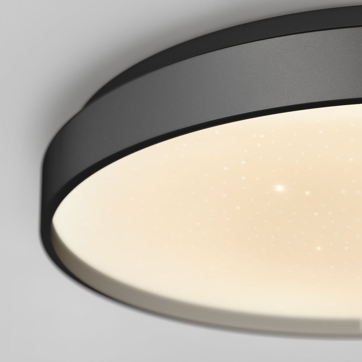 Close-up of a modern, circular ceiling light fixture with a black rim and a softly glowing, dotted surface, creating a star-like effect on the white diffuser.