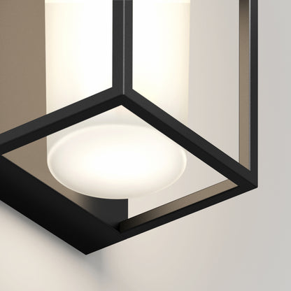 A close-up of the Sherman modern LED indoor-outdoor wall light by Artika, featuring a geometric black metal frame and frosted white bulb, mounted on a light-colored wall.