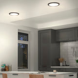 A modern kitchen with grey cabinets, white subway tile backsplash, and recessed ceiling lights. There is a window, kitchen utensils on the counter, and a table with chairs in the foreground.
