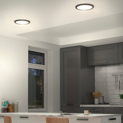 A modern kitchen with grey cabinets, white subway tile backsplash, and recessed ceiling lights. There is a window, kitchen utensils on the counter, and a table with chairs in the foreground.