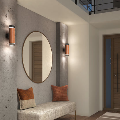 A modern entryway features a concrete accent wall, round mirror, Artika C7 indoor-outdoor LED wall lights, cushioned bench with two decorative pillows, and a wooden front door for a contemporary, inviting feel.