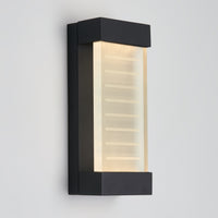 The Artika Percy LED indoor-outdoor wall light features a modern black rectangular frame and a frosted glass panel with horizontal etched lines, softly glowing against a plain light gray wall.