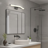 A modern bathroom with a square mirror, a curved LED light above it, a white vessel sink, black fixtures, a glass shower with a black rain showerhead, and a small plant on the counter.