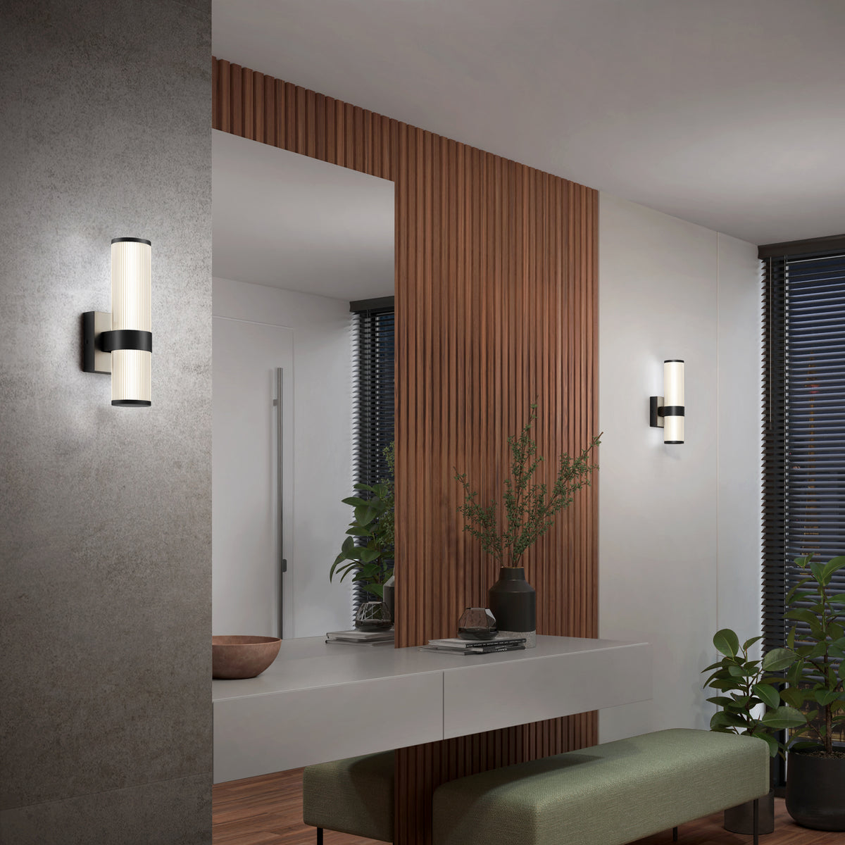 Modern entryway with a large mirror, wall-mounted lights, a sleek console table with decorative items, green plants, wood panel accents, and a bench.