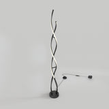 A modern floor lamp with three intertwined, twisting black and white light tubes, standing on a round black base with a power cord and switch lying on a plain light gray background.