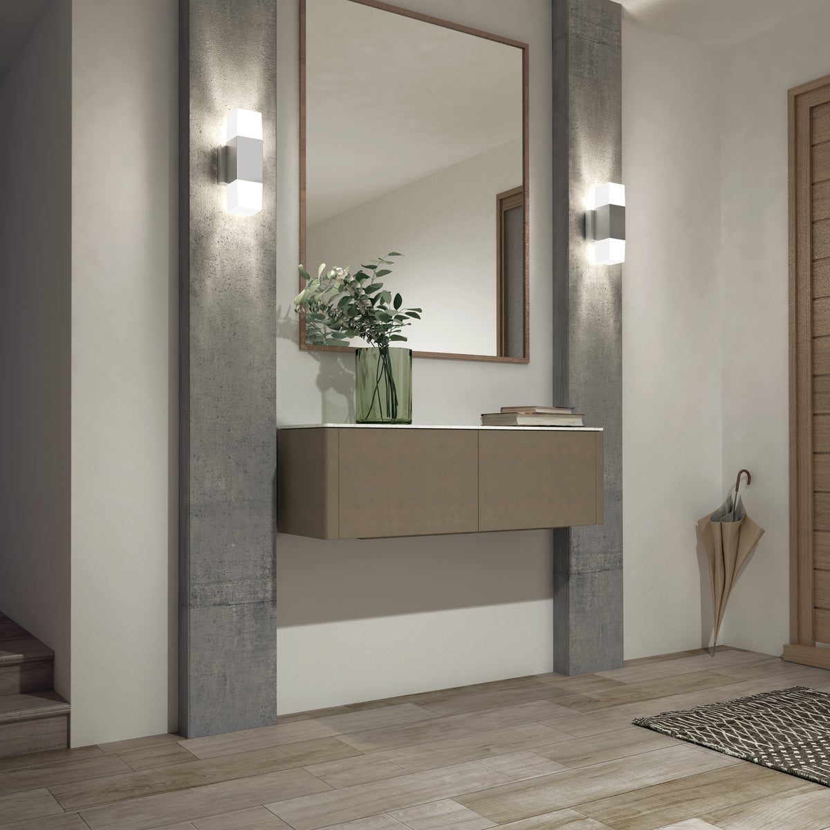 A modern entryway with a floating console, large mirror, green vase with leafy branches, wall sconces, tiled floor, woven rug, and a beige umbrella in a corner stand.