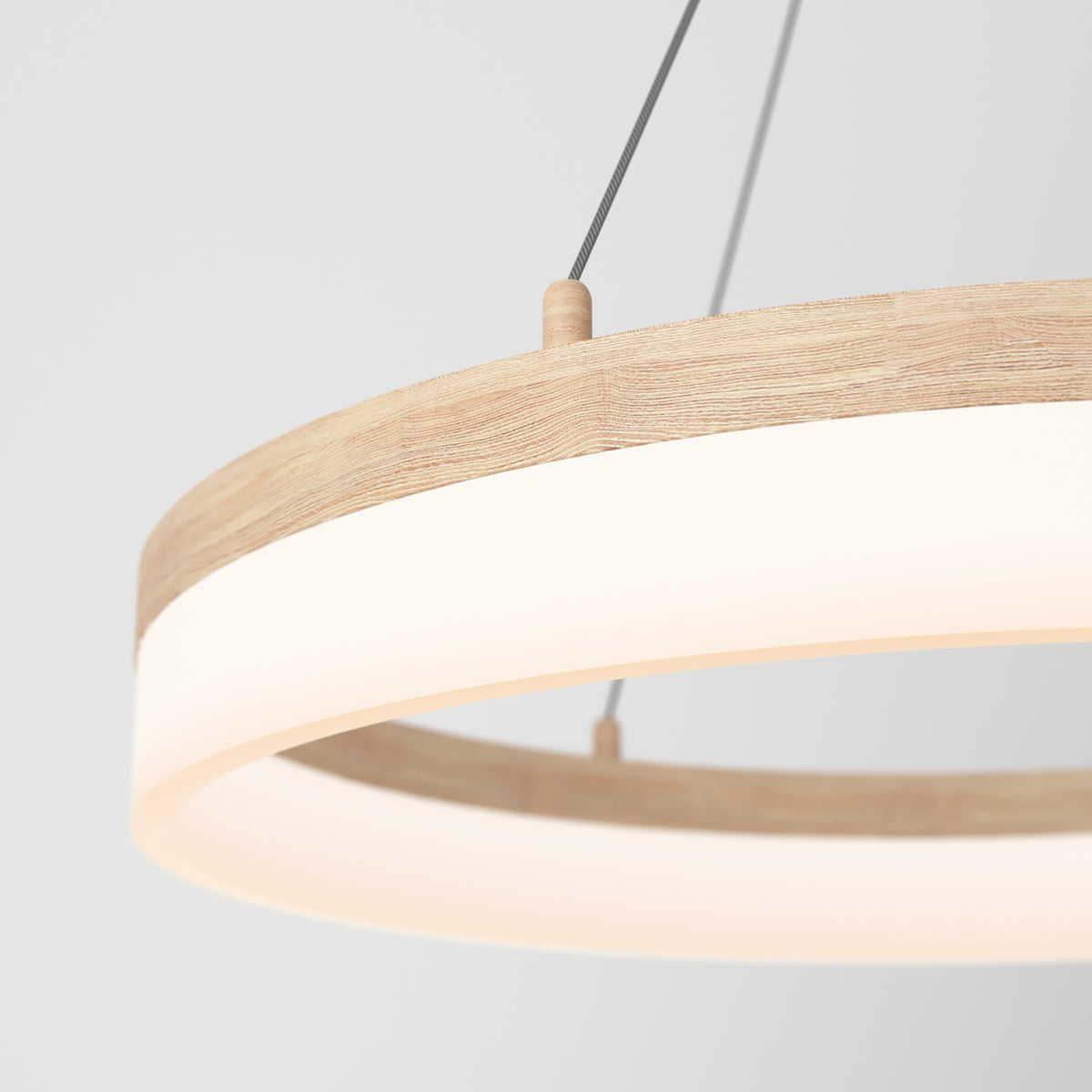 A close-up of a modern circular pendant light with a wooden frame and a glowing white diffuser, suspended by thin black cables against a plain white background.