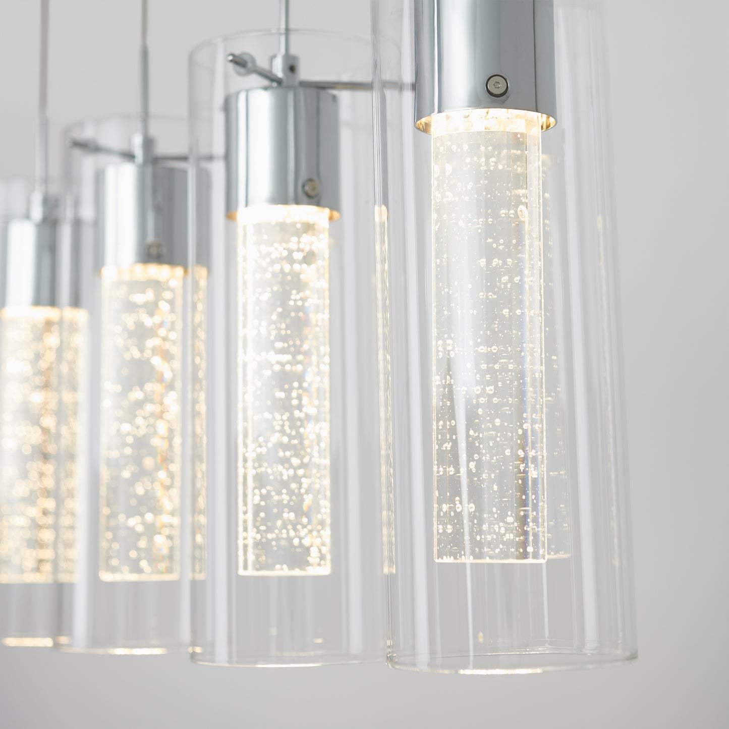 Close-up of the Essence 4-light LED pendant by Artika, featuring modern chrome fixtures and cylindrical clear glass shades with bubble-filled inner tubes illuminated by bright white light.