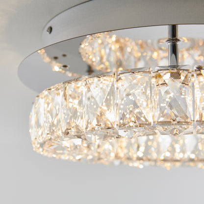 Close-up of the Artika Celebrity LED flush mount light, showcasing its circular design with rows of faceted crystal prisms on a sleek metallic frame, reflecting warm light against a light background.
