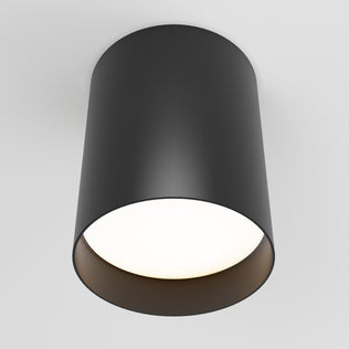 The Artika Radius LED flush mount light 3 CCT is a modern black cylindrical ceiling fixture with a smooth matte finish, mounted on a white ceiling and emitting a soft white glow.