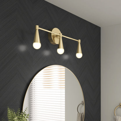 The Artika Wayden LED mid-century bathroom vanity light 3 CCT with gold finish and cone-shaped shades is mounted above a round mirror on a dark chevron-patterned bathroom wall, reflecting light on both the wall and mirror.