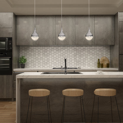 Modern kitchen with grey wood cabinets, hexagonal white tile backsplash, and an Artika Glitzer LED pendant light over a white island countertop with a black sink and three wooden bar stools. Green plant and kitchen items are on the counter.